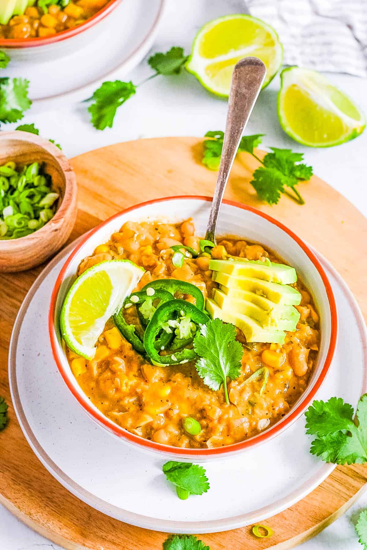 Vegan white bean chili topped with avocado, jalapeno slices and lime in a white bowl with a spoon.