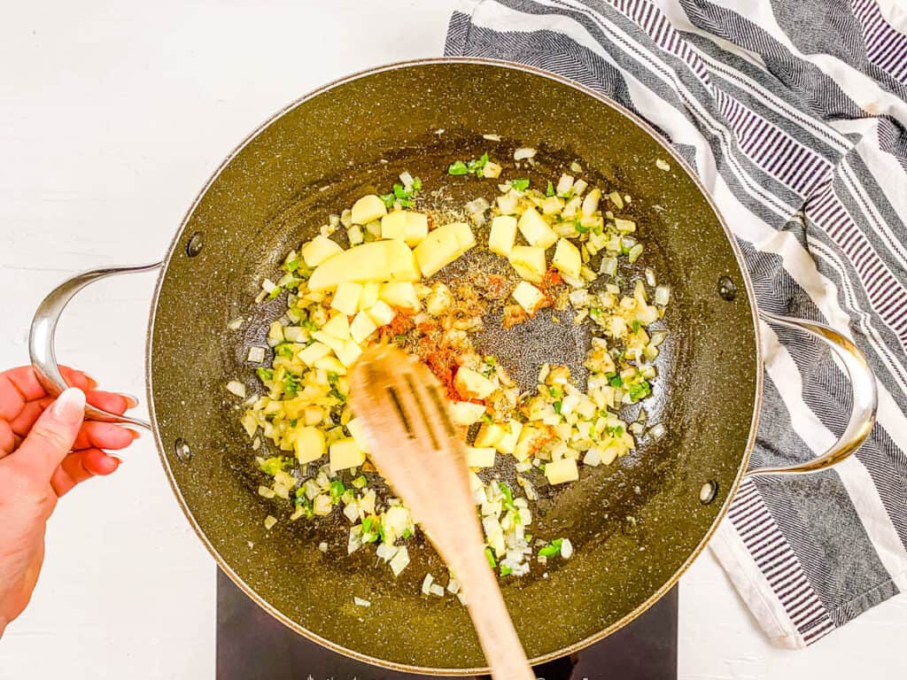 Potatoes and spices sauteeing in a stock pot.