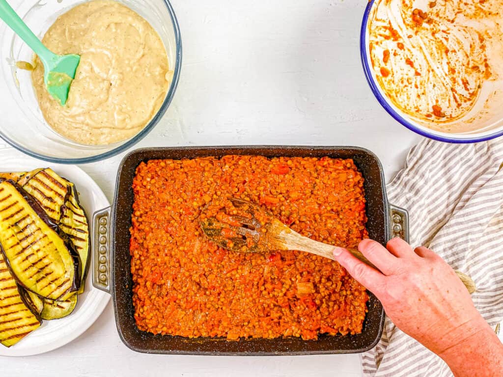 Vegan lentil ragu added to vegetarian moussaka recipe in a baking dish.