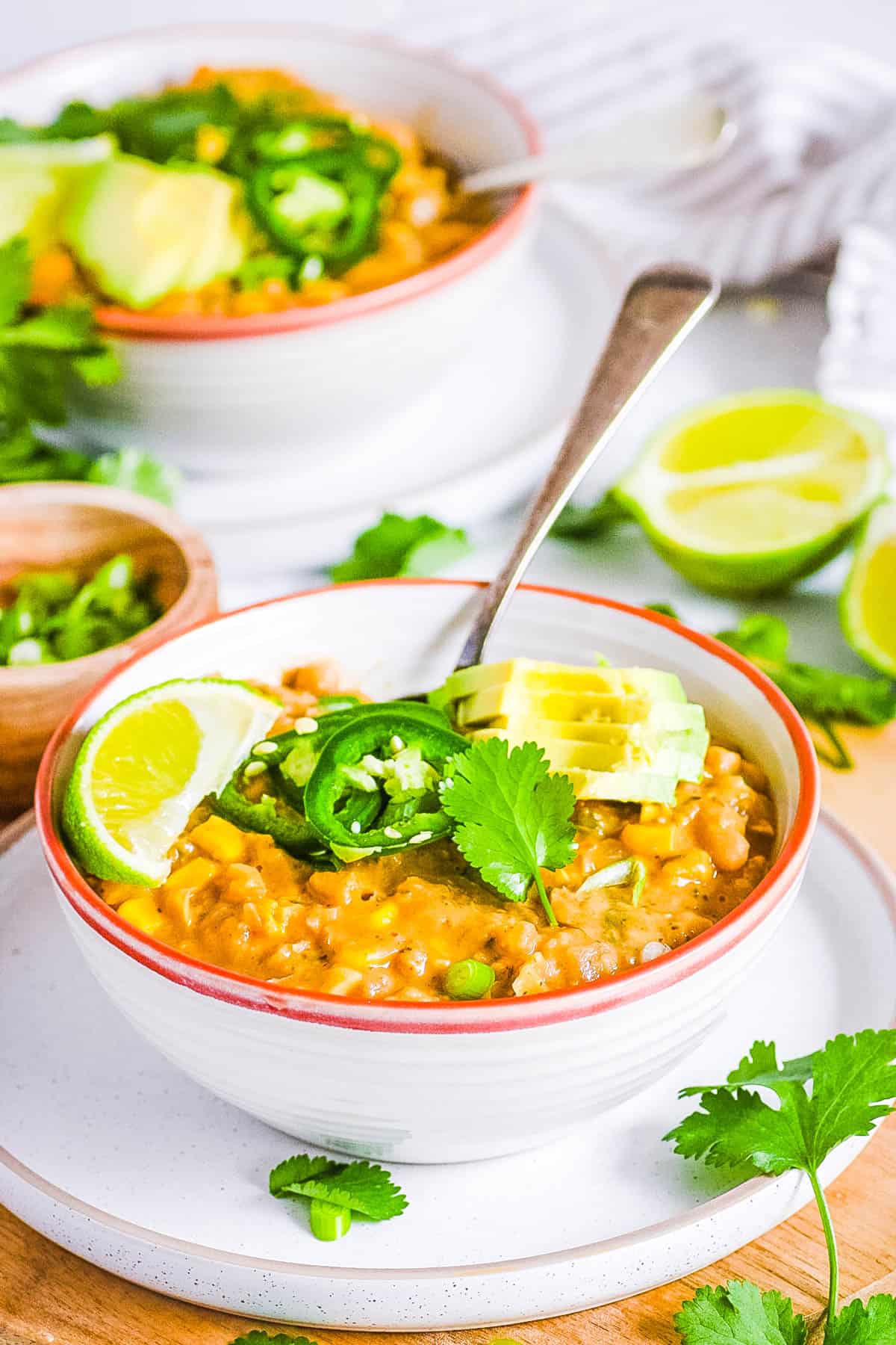 Vegan white bean chili topped with avocado, jalapeno slices and lime in a white bowl with a spoon.