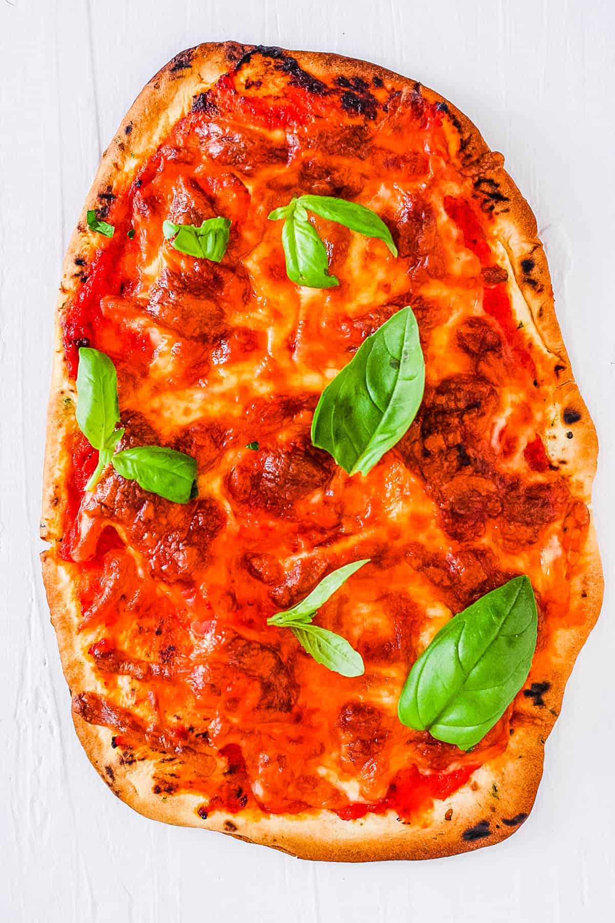 Margarita naan bread pizza topped with mozzarella and basil, on a white cutting board.