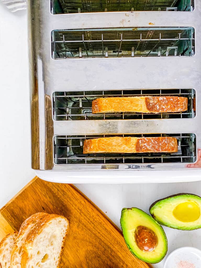 Sourdough toast in a toaster with avocado on the side.