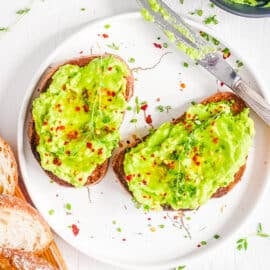 Avocado toast with honey and red chili flakes on a white plate.