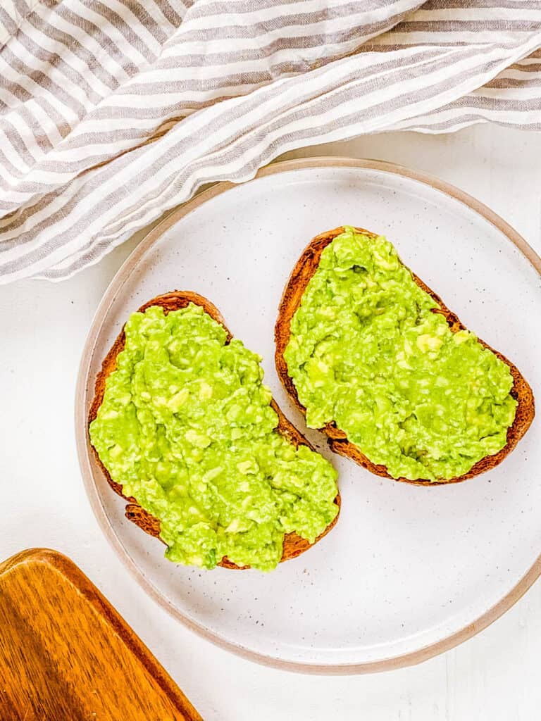 Mashed avocado spread on sourdough bread on a white plate.