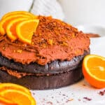 Chocolate orange cake topped with orange slices and a chocolate ganache frosting on a white cake board.