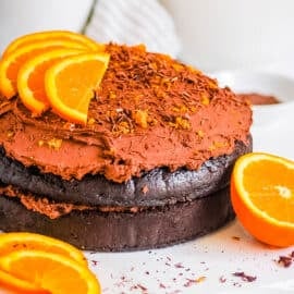 Chocolate orange cake topped with orange slices and a chocolate ganache frosting on a white cake board.
