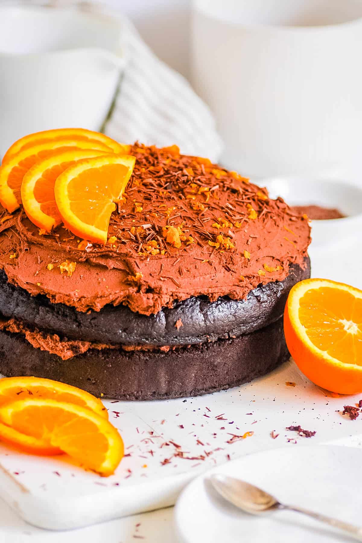 Chocolate orange cake topped with orange slices and a chocolate ganache frosting on a white cake board.