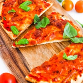 Crispy naan bread pizza topped with mozzarella and basil, on a wooden cutting board.