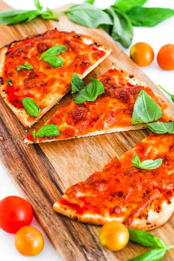 Crispy naan bread pizza topped with mozzarella and basil, on a wooden cutting board.