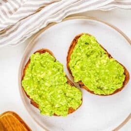 Mashed avocado spread on sourdough bread on a white plate.
