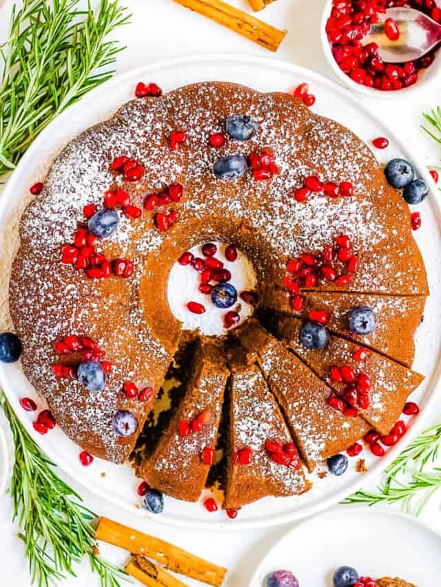 Gingerbread bundt cake topped with powdered sugar and fresh fruit on a white plate.