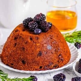 Traditional English vegan Christmas pudding topped with berries on a white plate.