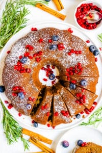 Gingerbread bundt cake topped with powdered sugar and fresh fruit on a white plate.