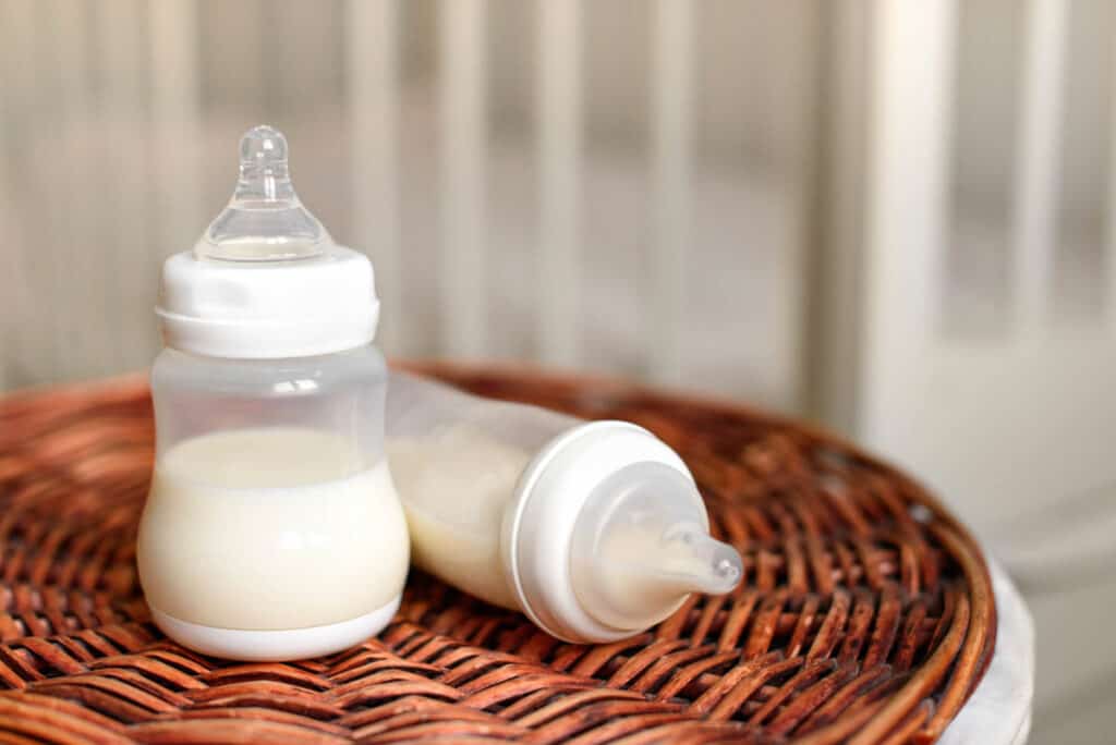 Baby bottles with milk for baby on a straw basket.