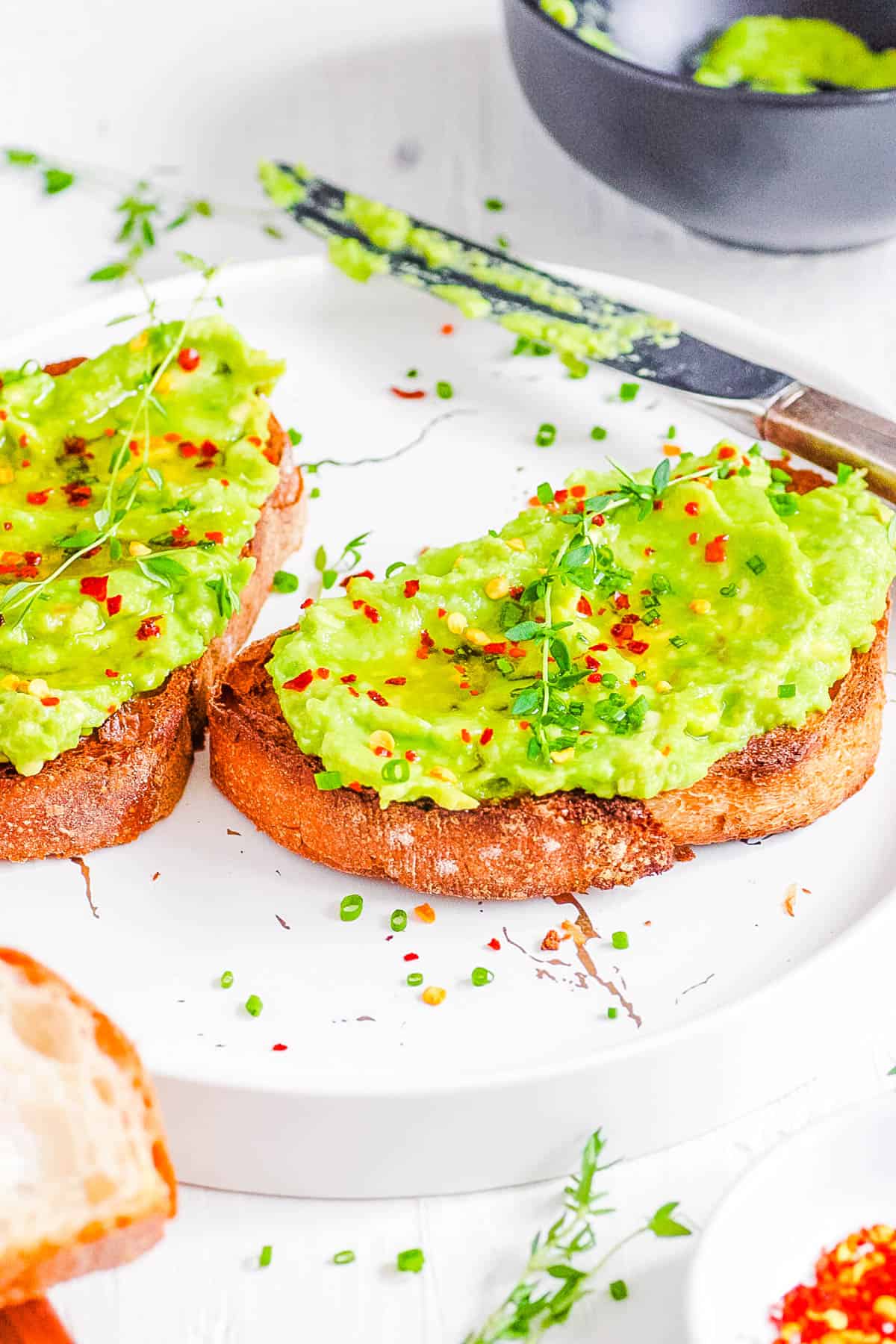 Honey avocado toast with chili flakes on a white plate.