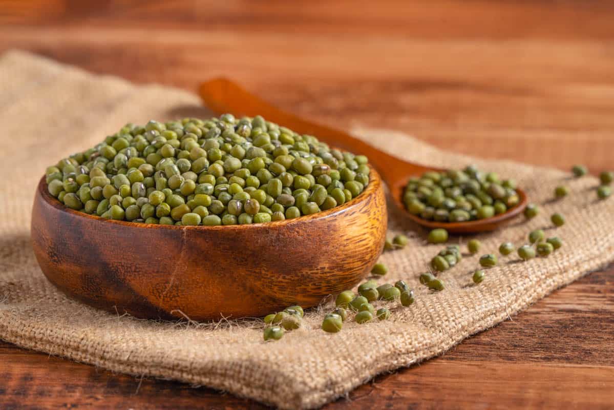 Close up of raw mung beans in a bowl on a wooden table.