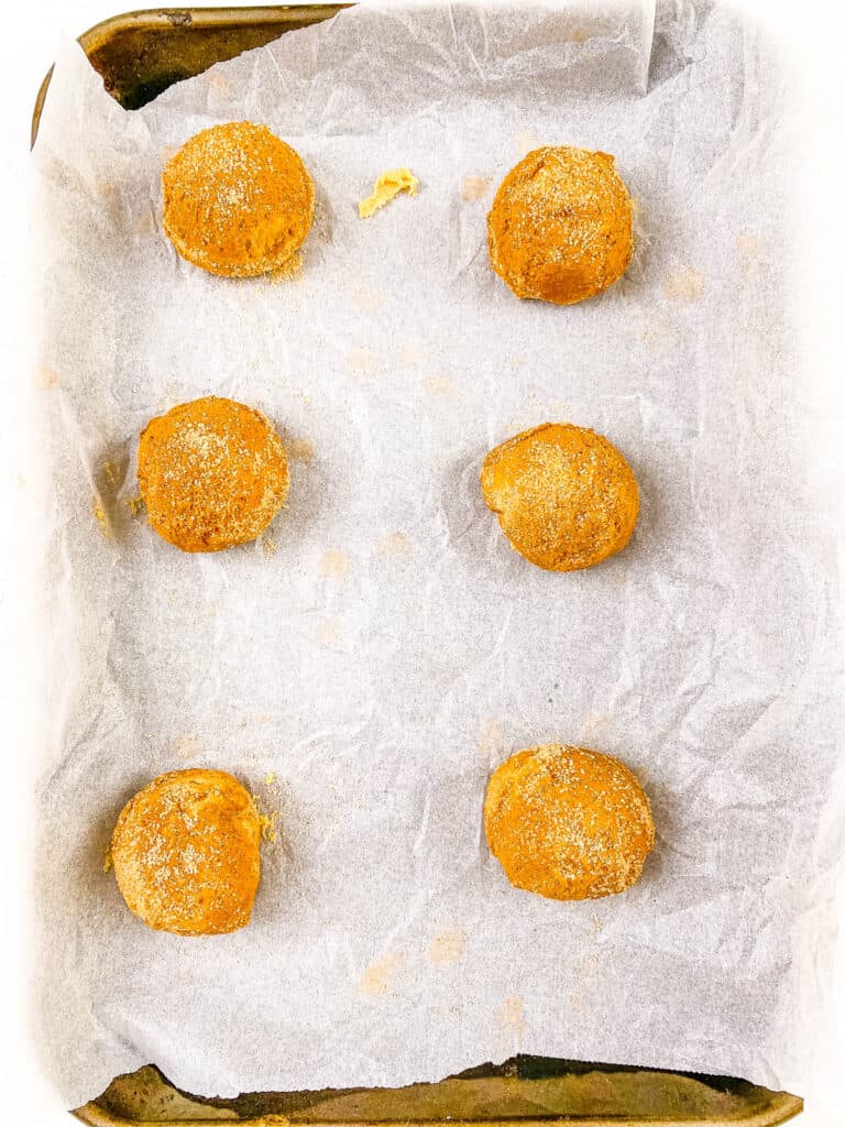Cookie dough balls rolled in cinnamon sugar on a baking sheet lined with parchment paper.