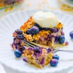 One slice of vegan baked oatmeal with blueberries topped with vegan whipped cream on a white plate.