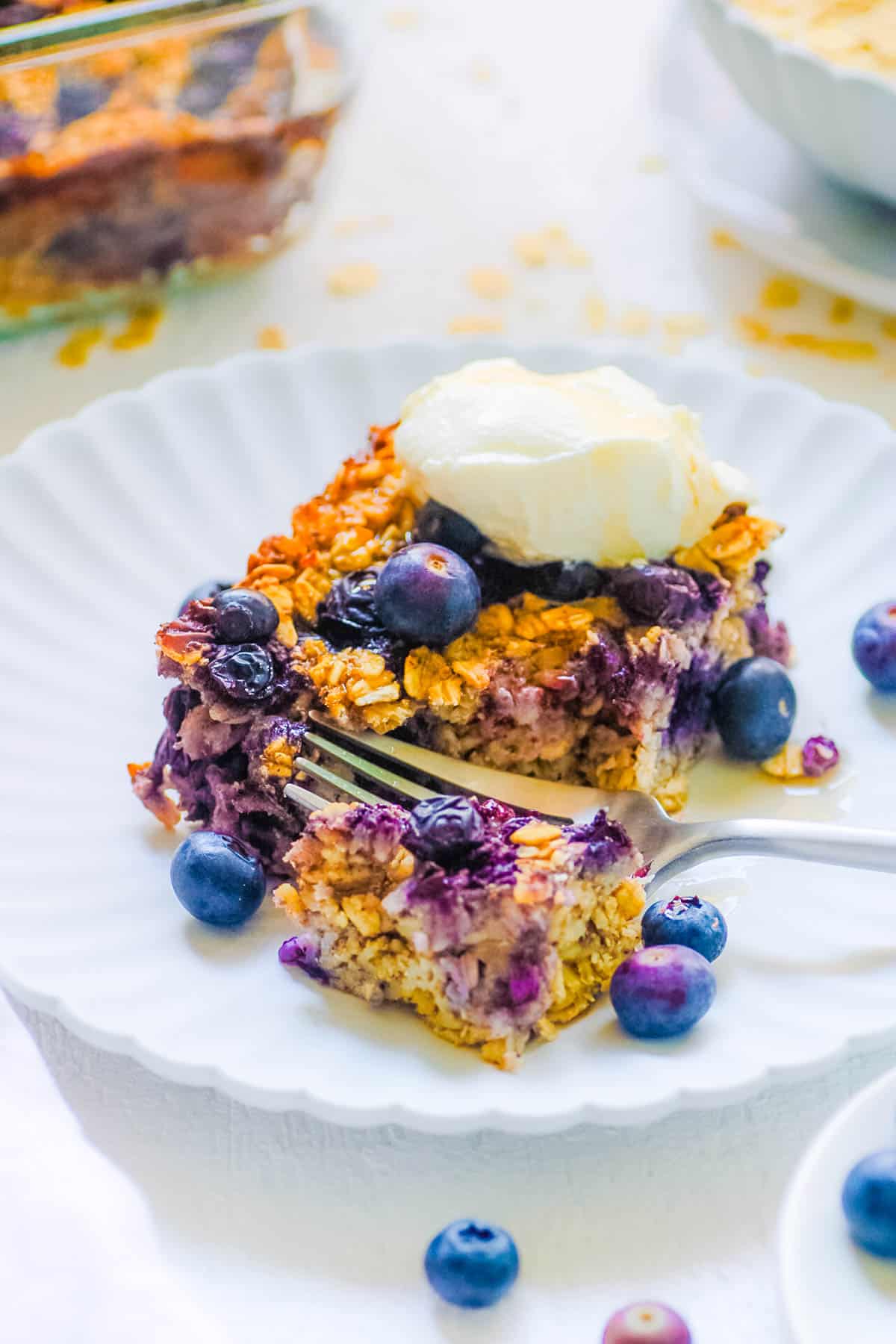 One slice of vegan baked oatmeal with blueberries topped with vegan whipped cream on a white plate.