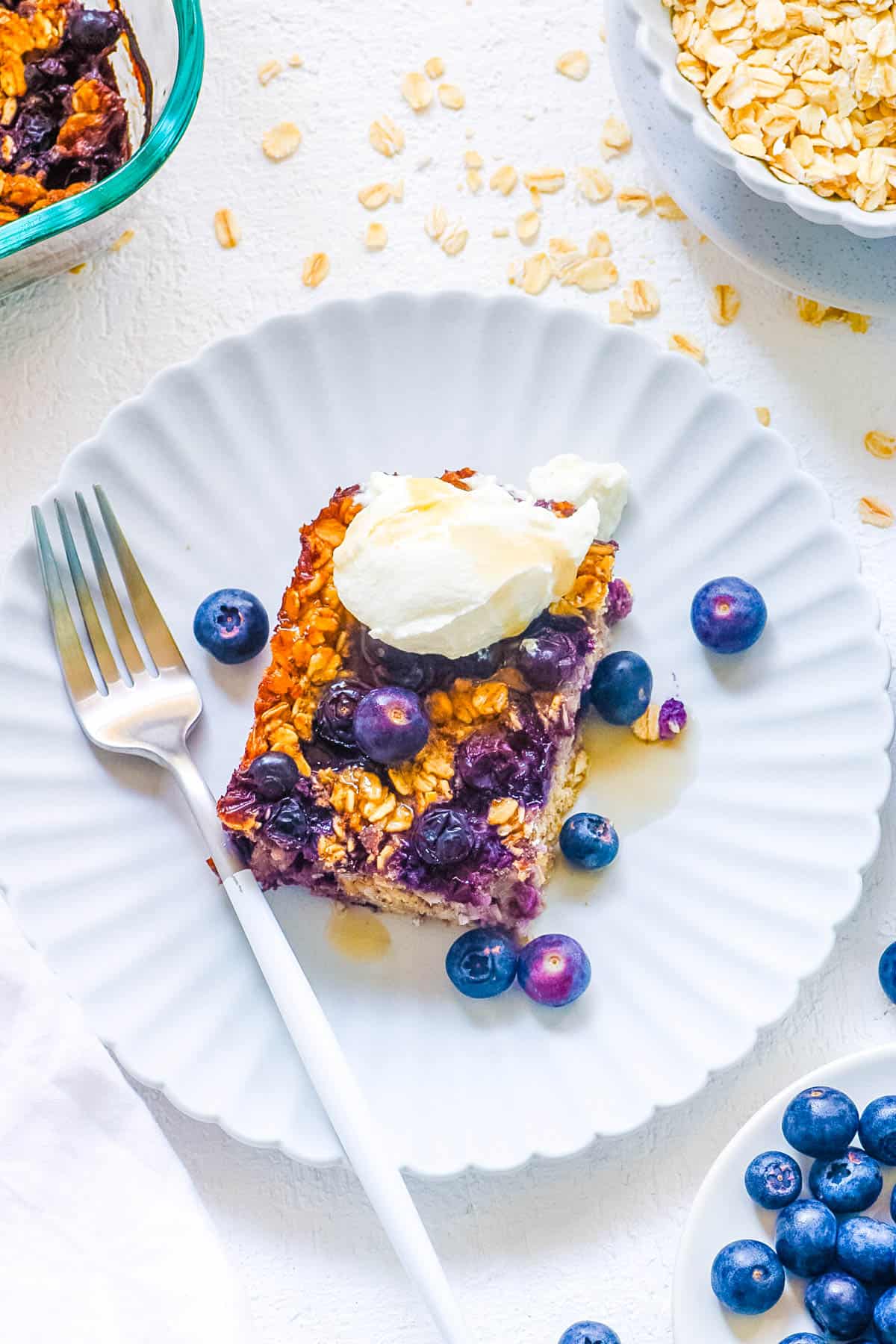 One slice of vegan baked oatmeal with blueberries topped with vegan whipped cream on a white plate.