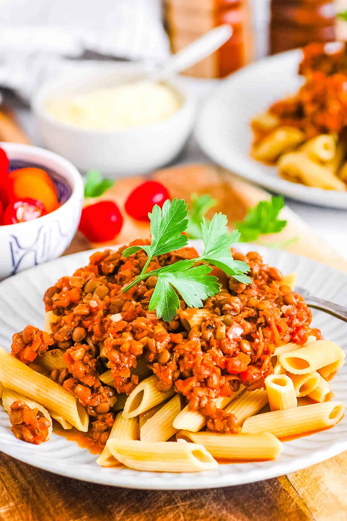 Vegan bolognese with lentils on top of penne pasta, on a white plate with a parsley garnish.