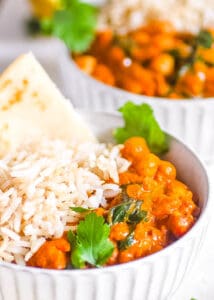 Chickpea and lentil curry served with rice and naan in a white bowl.