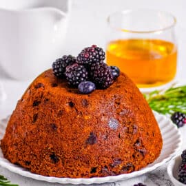 Traditional English vegan Christmas pudding topped with berries on a white plate.