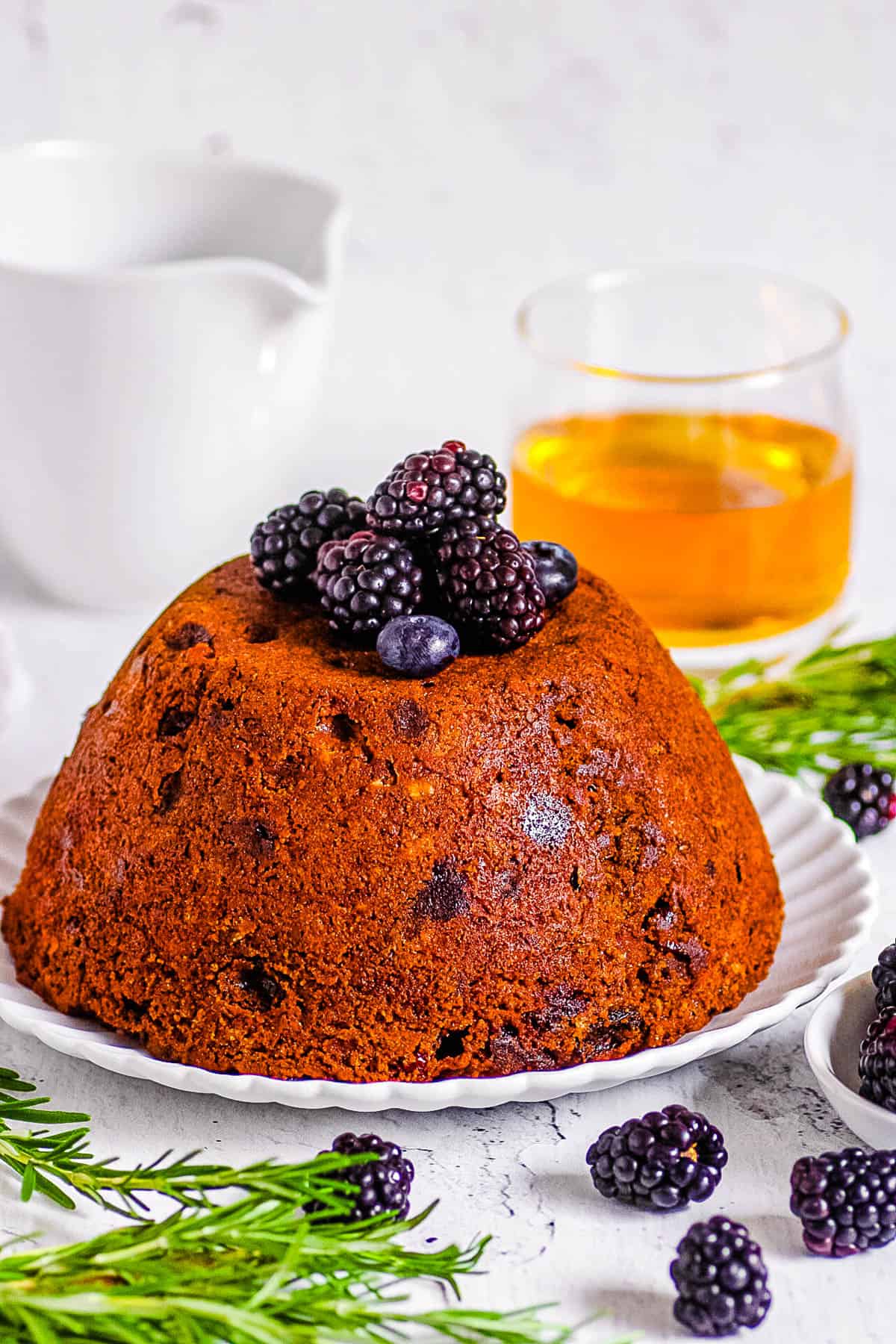 Traditional English vegan Christmas pudding topped with berries on a white plate.
