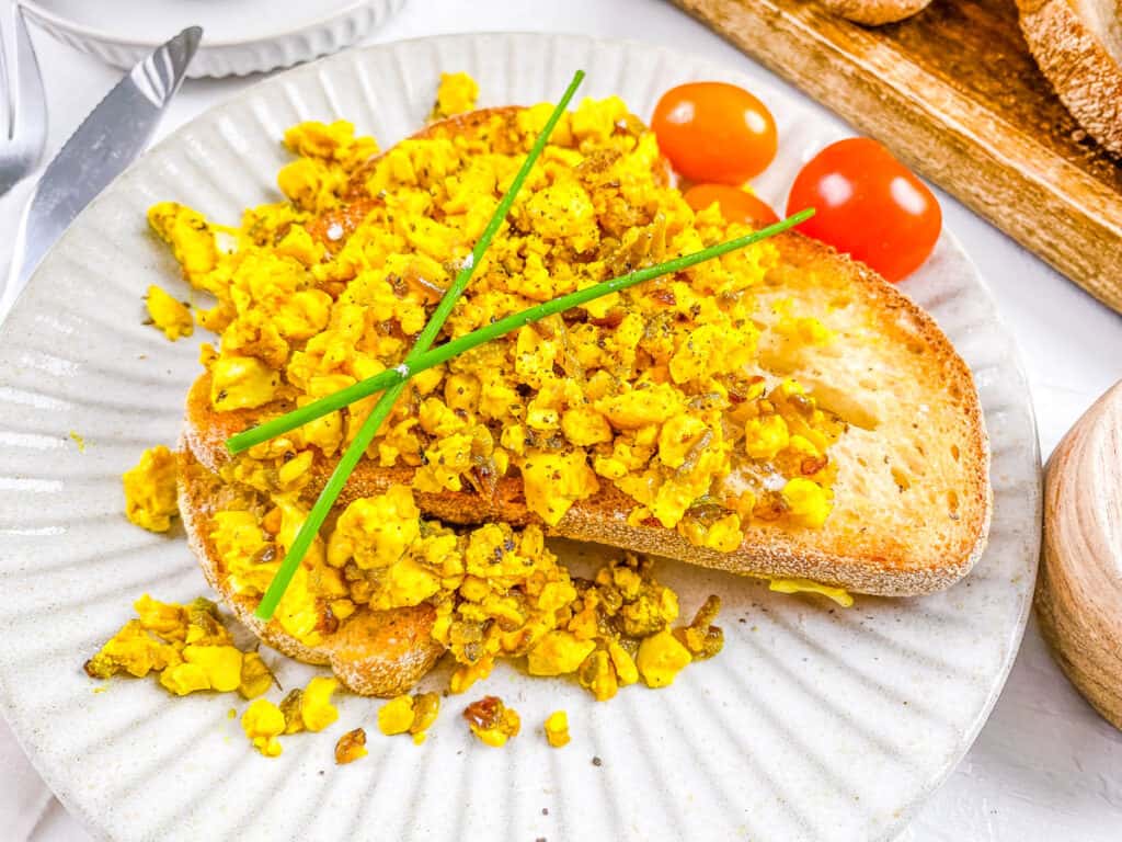 Vegan scrambled eggs with silken tofu on slices of toast, served on a white plate.