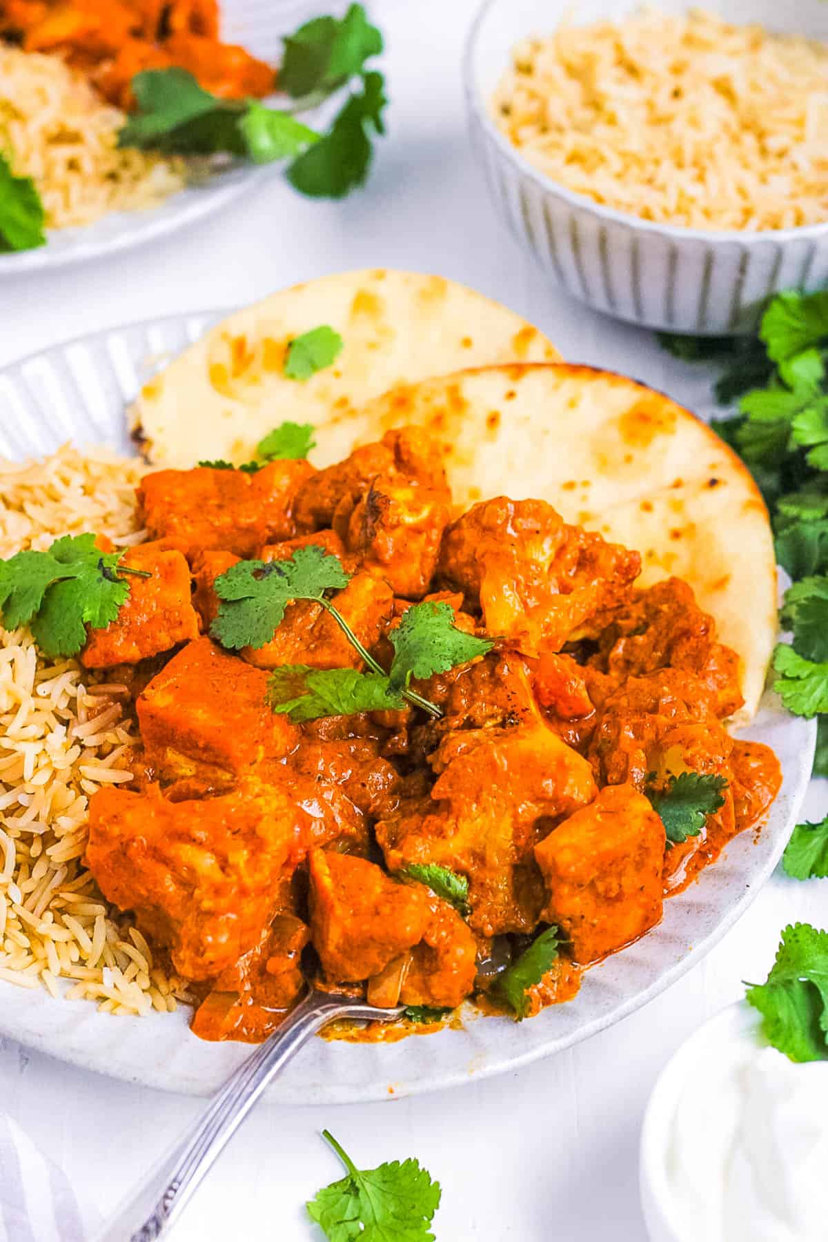 Vegan tikka masala served with rice and naan on a white plate.