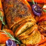 Vegan turkey roast in a serving dish with roasted vegetables surrounding it.