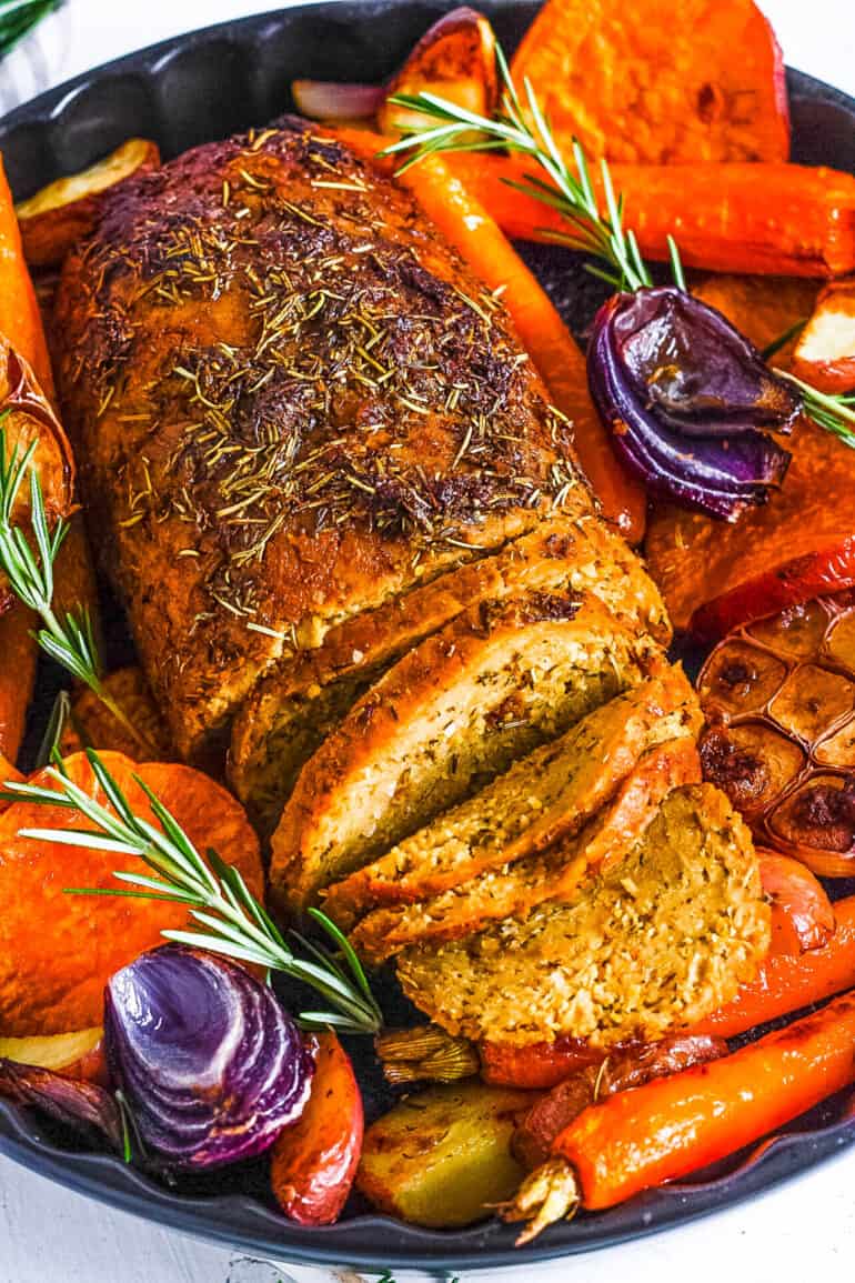 Vegan turkey roast in a serving dish with roasted vegetables surrounding it.