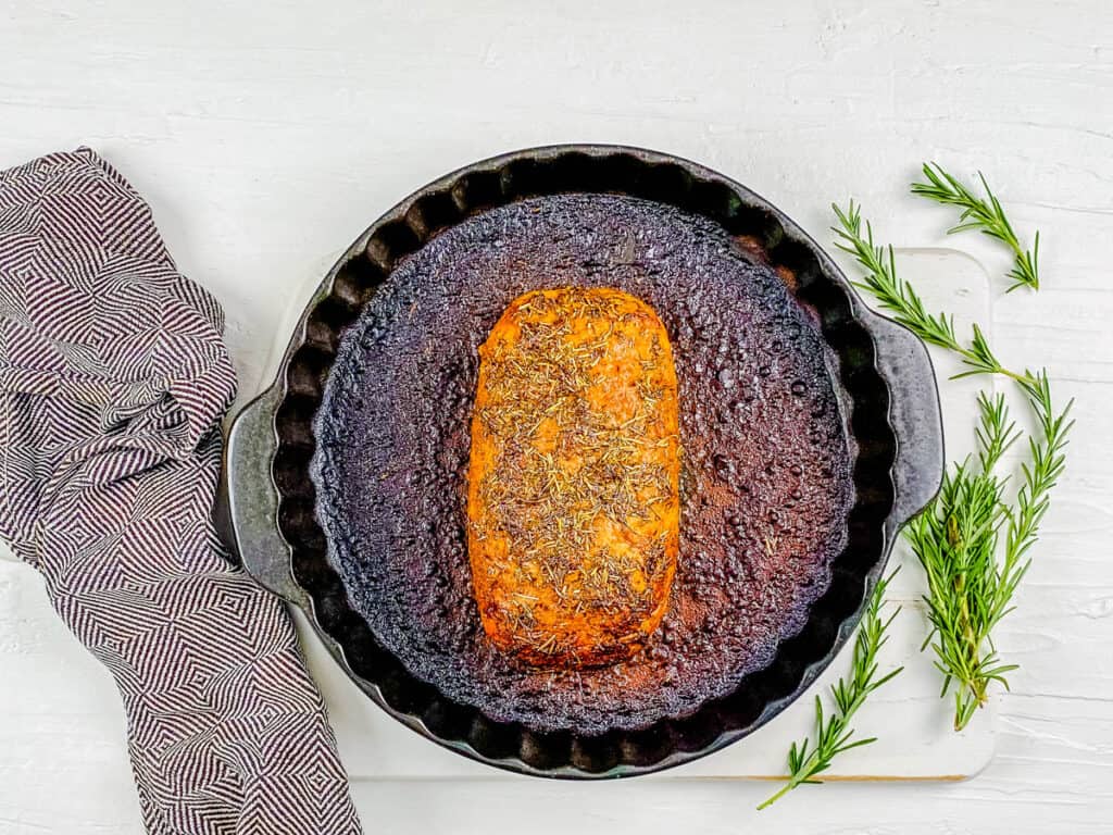 Vegan roast turkey in a baking dish with basting liquid.