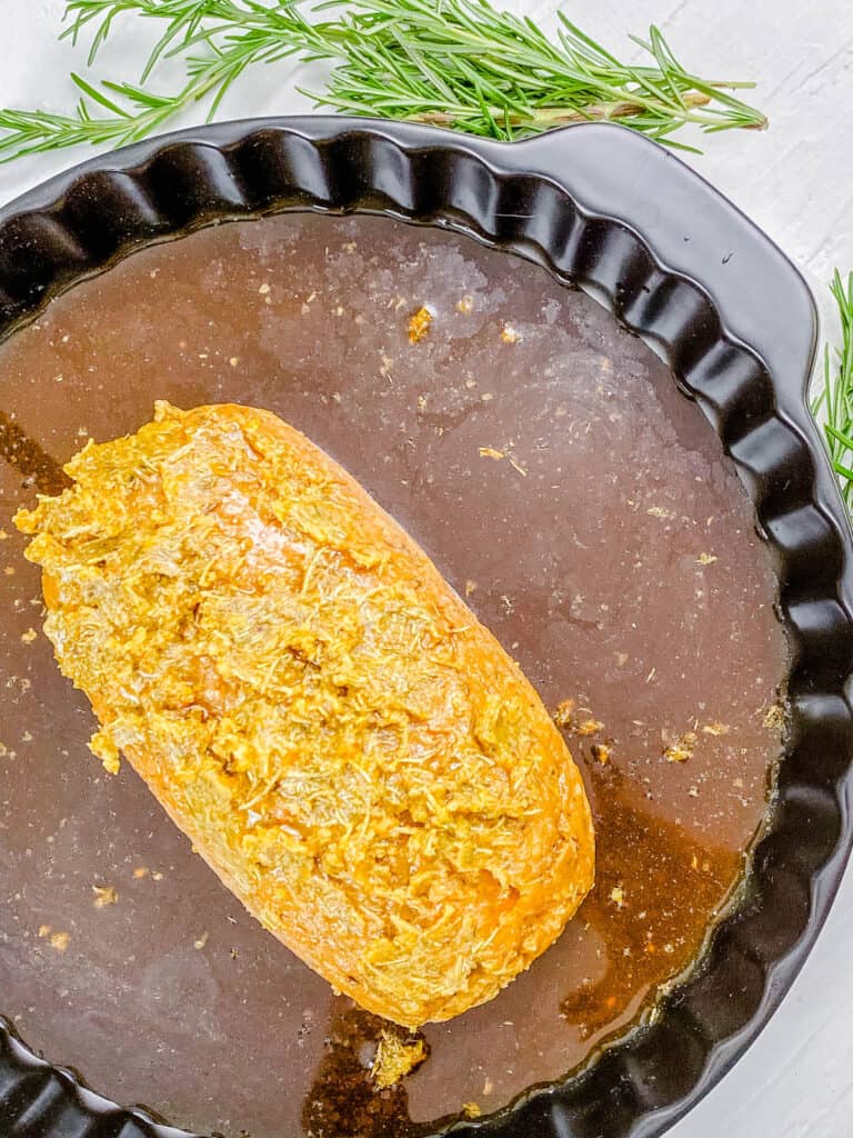 Seitan turkey loaf in a baking dish surrounded by basting liquid.