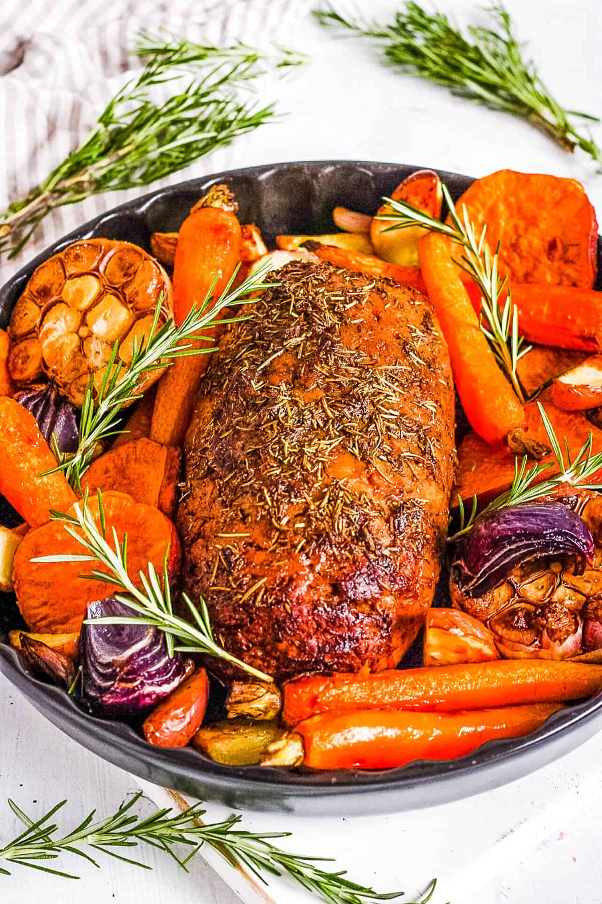 Vegan turkey roast in a serving dish with roasted vegetables surrounding it.