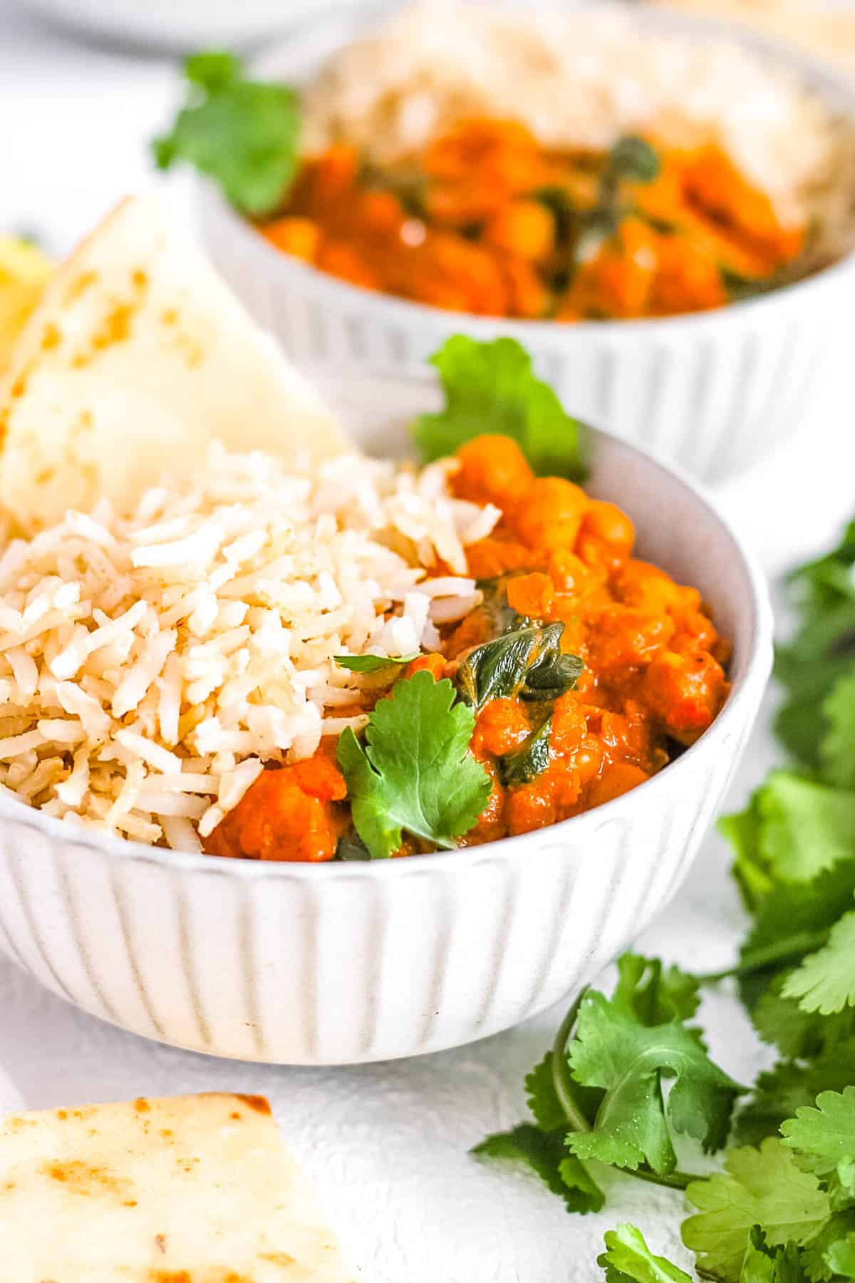 Vegan chickpea and lentil curry served with rice and naan in a white bowl.