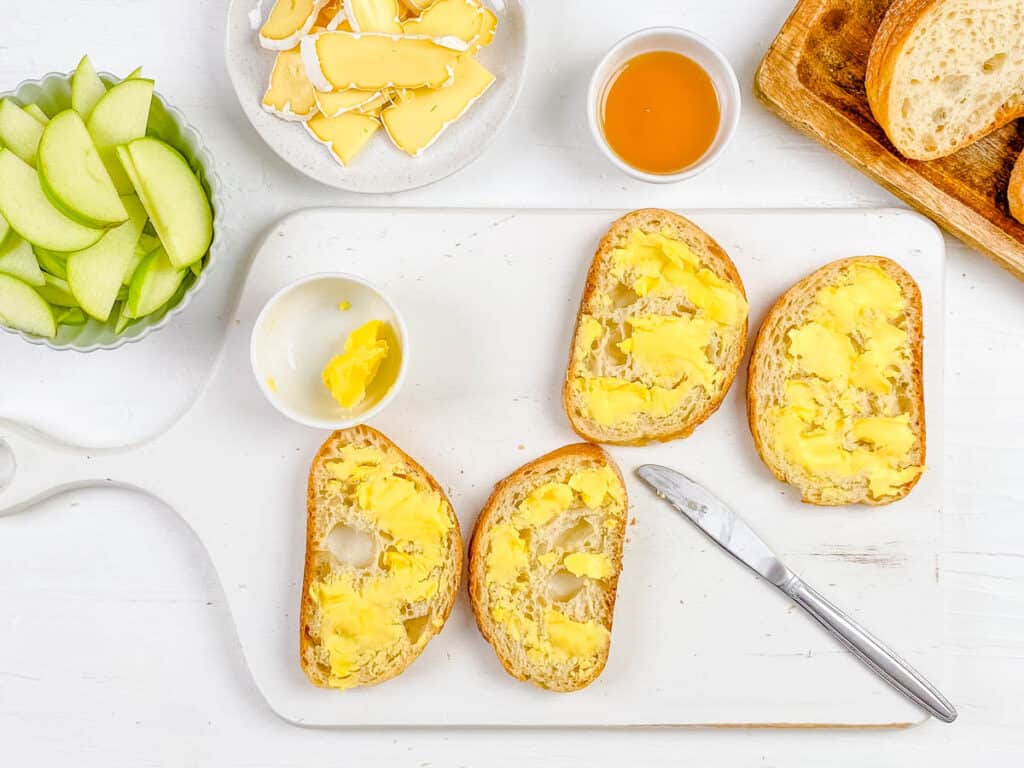 Butter spread on slices of sourdough bread on a cutting board.