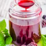 Homemade blackberry simple syrup recipe in a gl، jar with fresh herbs and blackberries on the side.