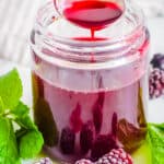 Homemade blackberry simple syrup recipe in a glass jar with fresh herbs and blackberries on the side.