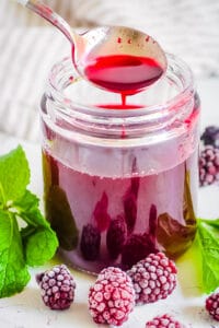 Homemade blackberry simple syrup recipe in a glass jar with fresh herbs and blackberries on the side.