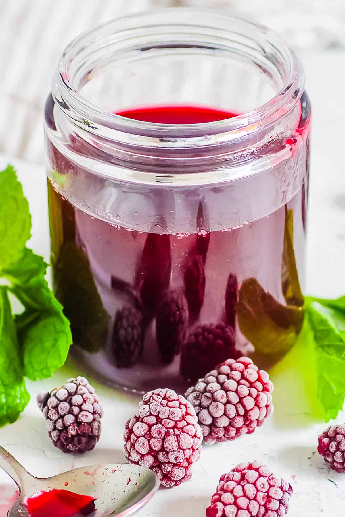 Easy blackberry simple syrup recipe in a glass jar with fresh herbs and blackberries on the side.