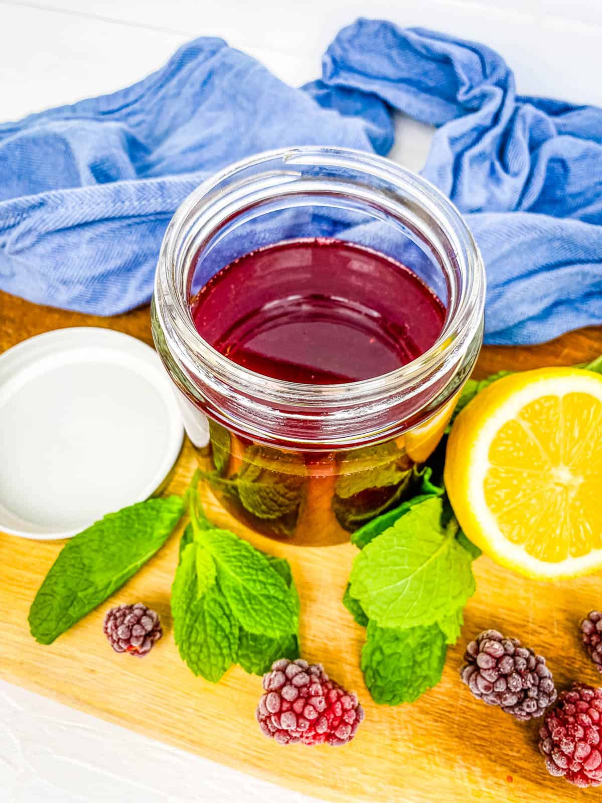 Blackberry syrup for drinks stored in a mason jar on a wooden cutting board.