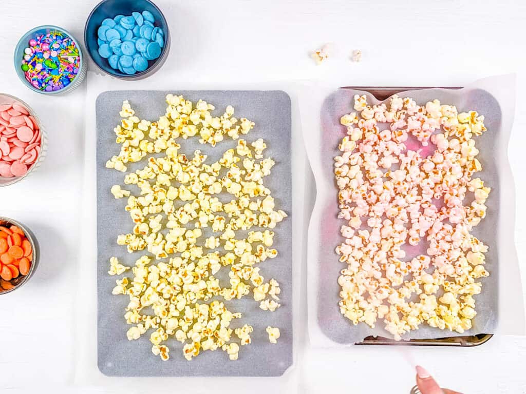Candy melt popcorn sprayed with pink food coloring on a baking sheet.