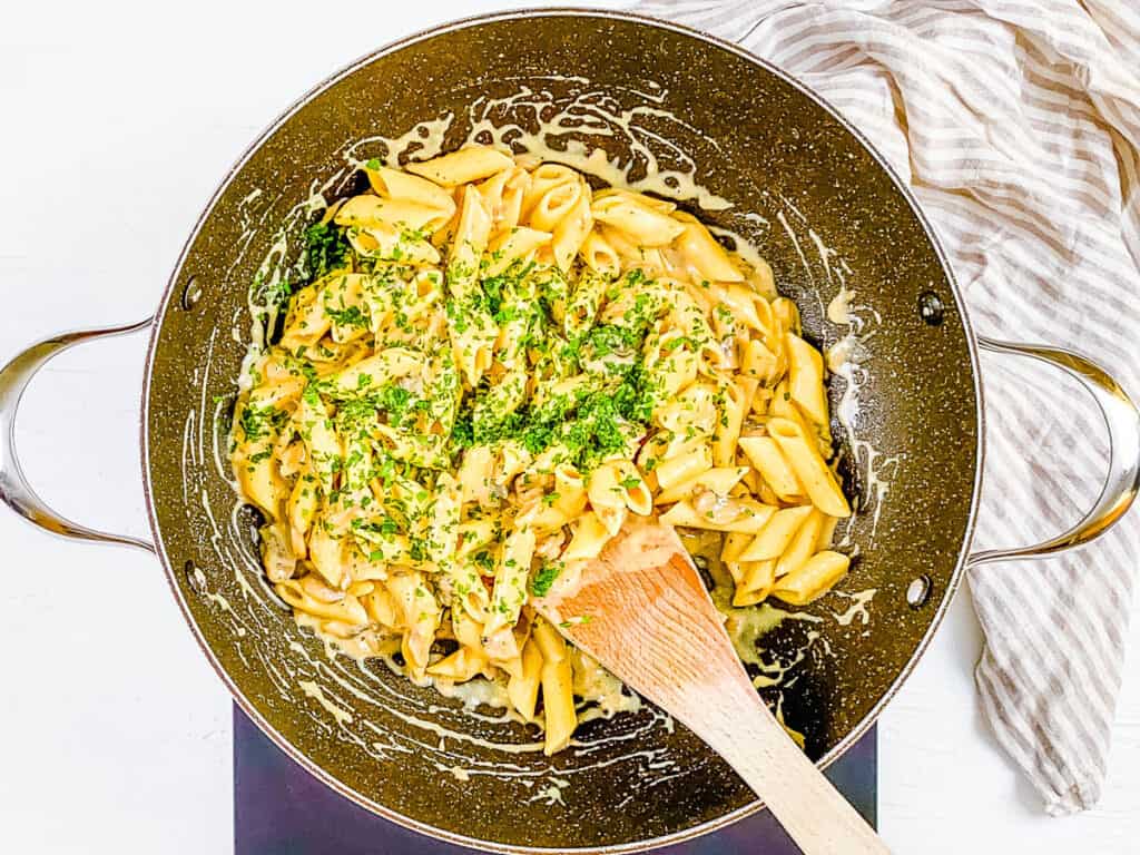 Creamy mushroom vegan pasta cooking in a pan, topped with fresh herbs.
