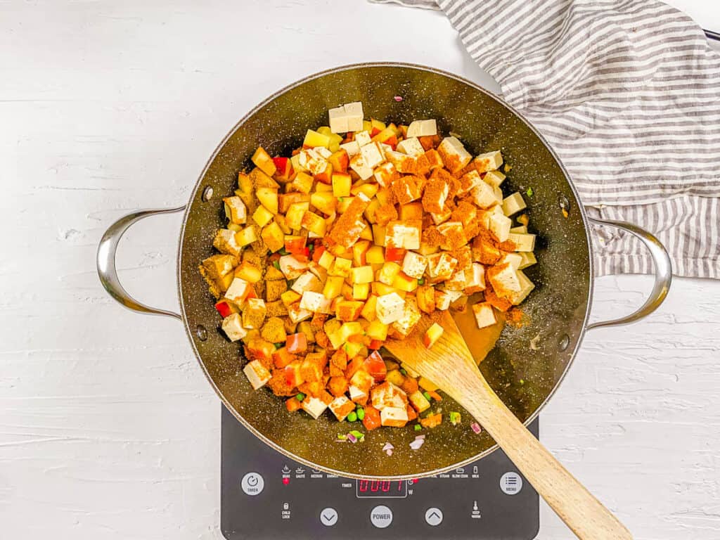 Tofu, potatoes, and spices cooking in a pan.