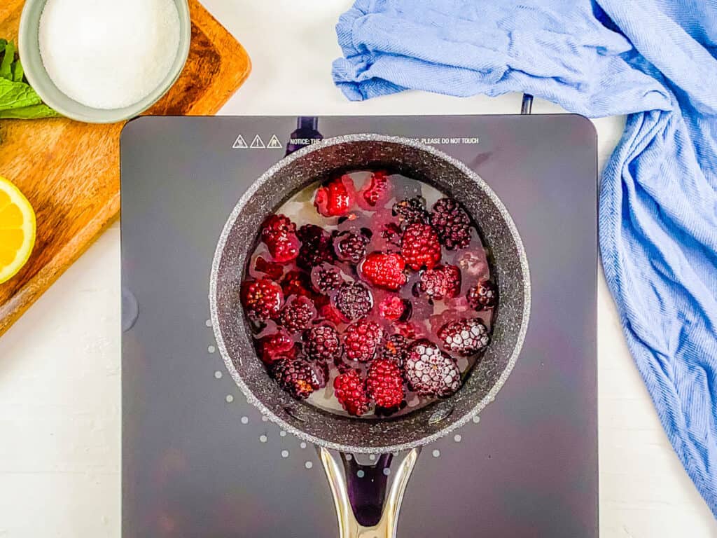 Blackberries, sugar, water, and lemon being cooked in a large pot.