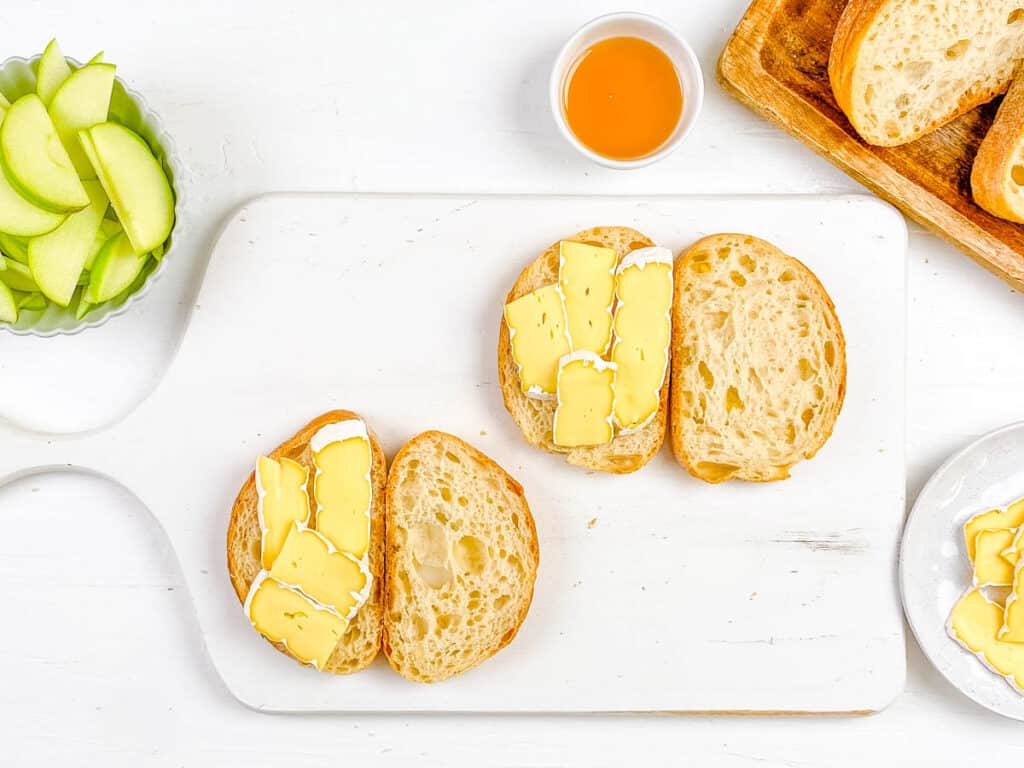 Brie added to slices of sourdough bread on a cutting board.