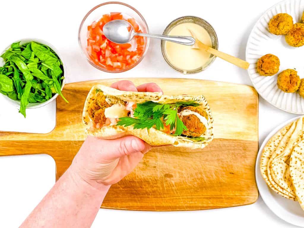 A hand holding a vegan falafel wrap over a cutting board.