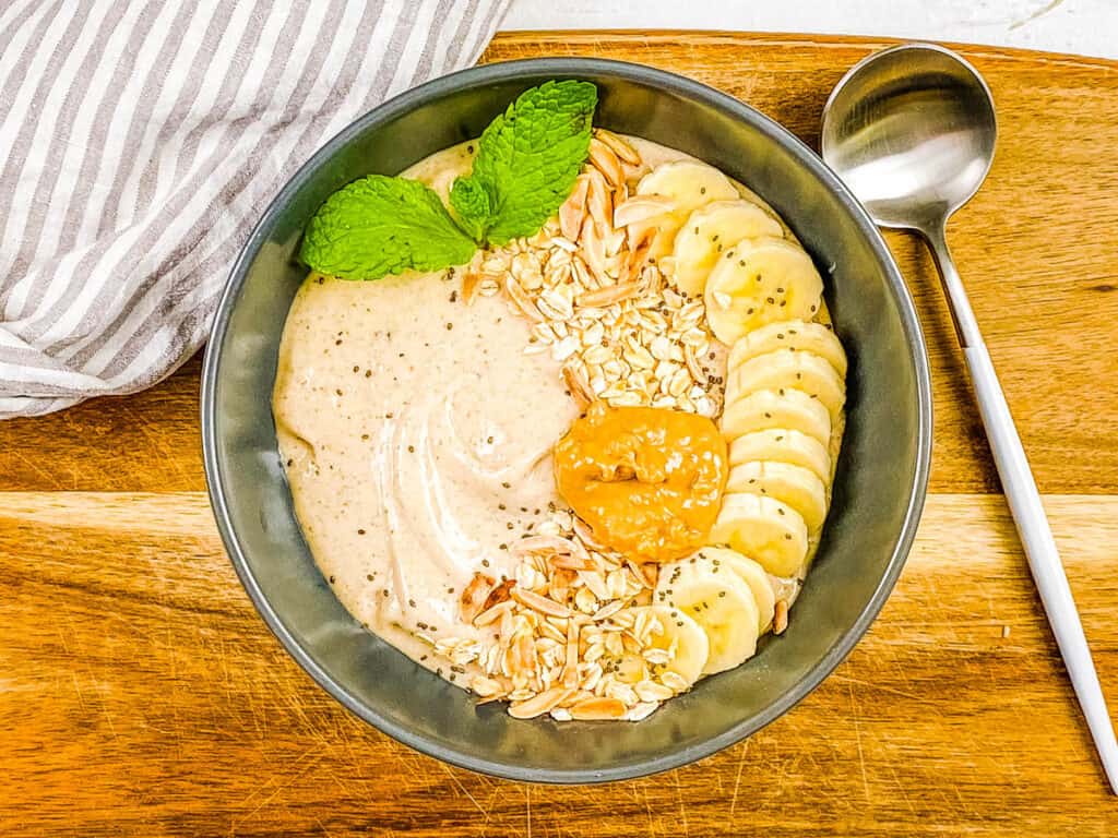 Banana bowl with toppings - banana slices, nuts, seeds, nut butter in a grey bowl.