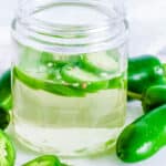 Jalapeno simple syrup in a gl، mason jar, garnished with jalapeno slices.